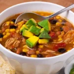 Warm bowl of chicken taco soup on a rustic table, symbolizing the popularity of this comforting dish.