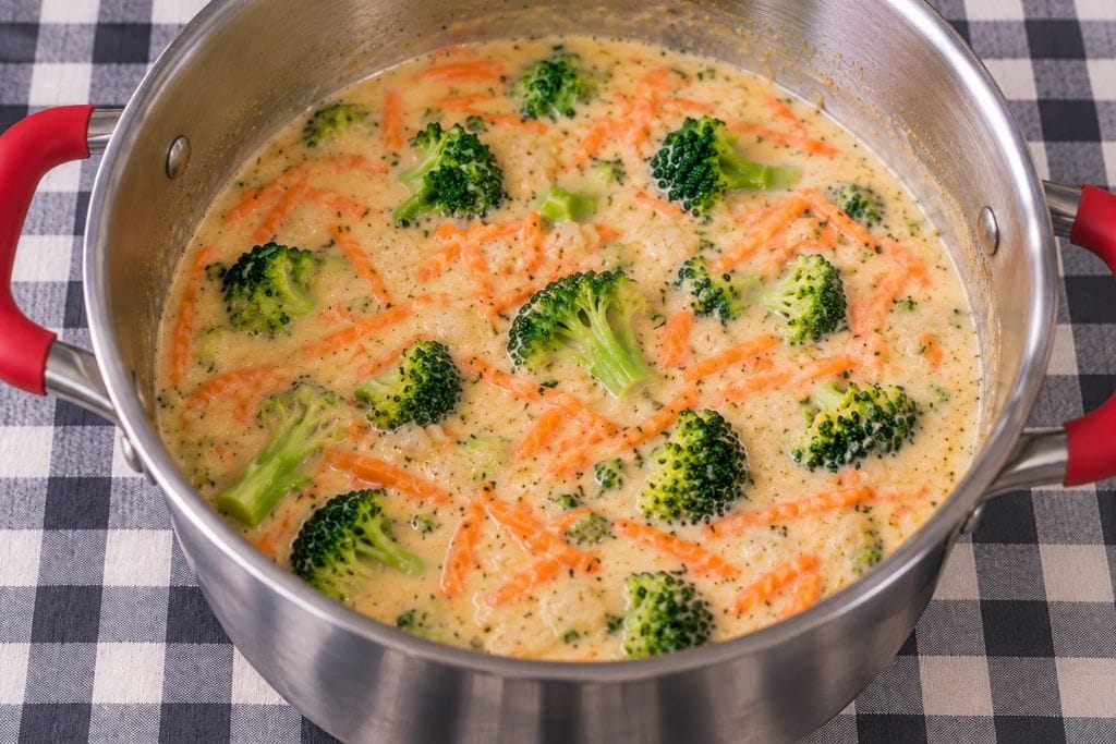 Broccoli florets and carrots simmering in creamy broth before adding cheese