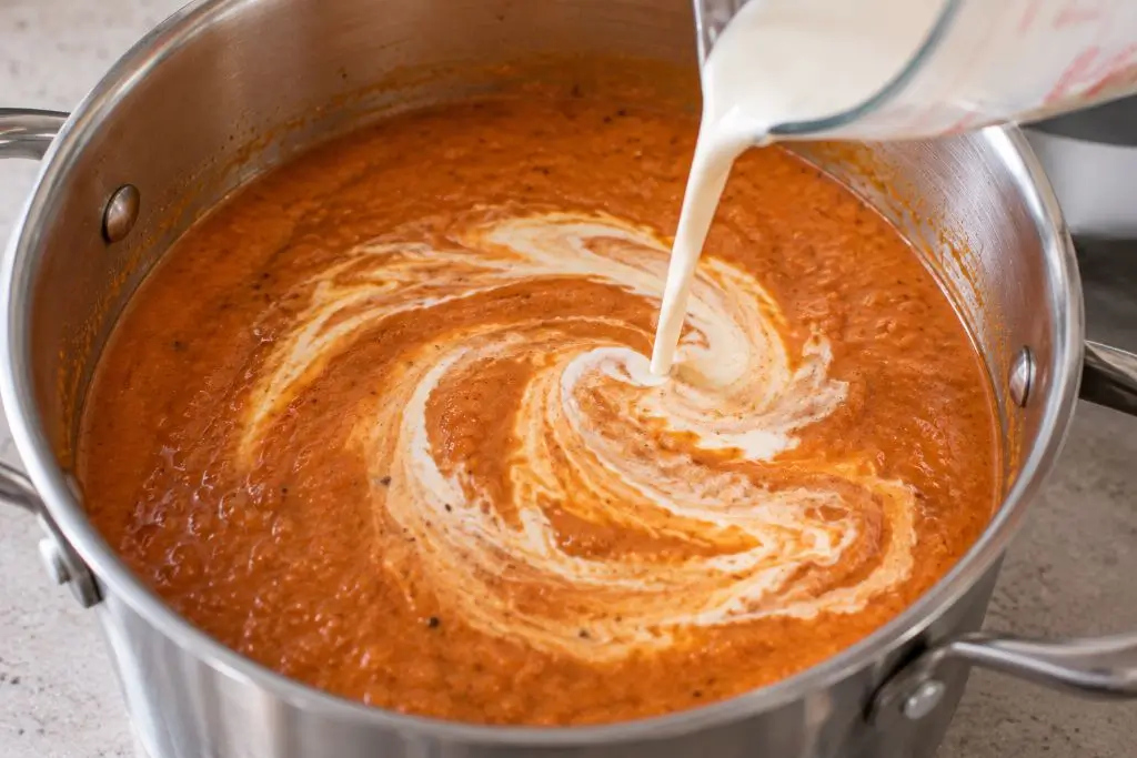 Cream being poured and swirled into creamy tomato basil soup off the heat