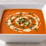 Bowl of creamy tomato basil soup topped with a swirl of cream and fresh basil leaves
