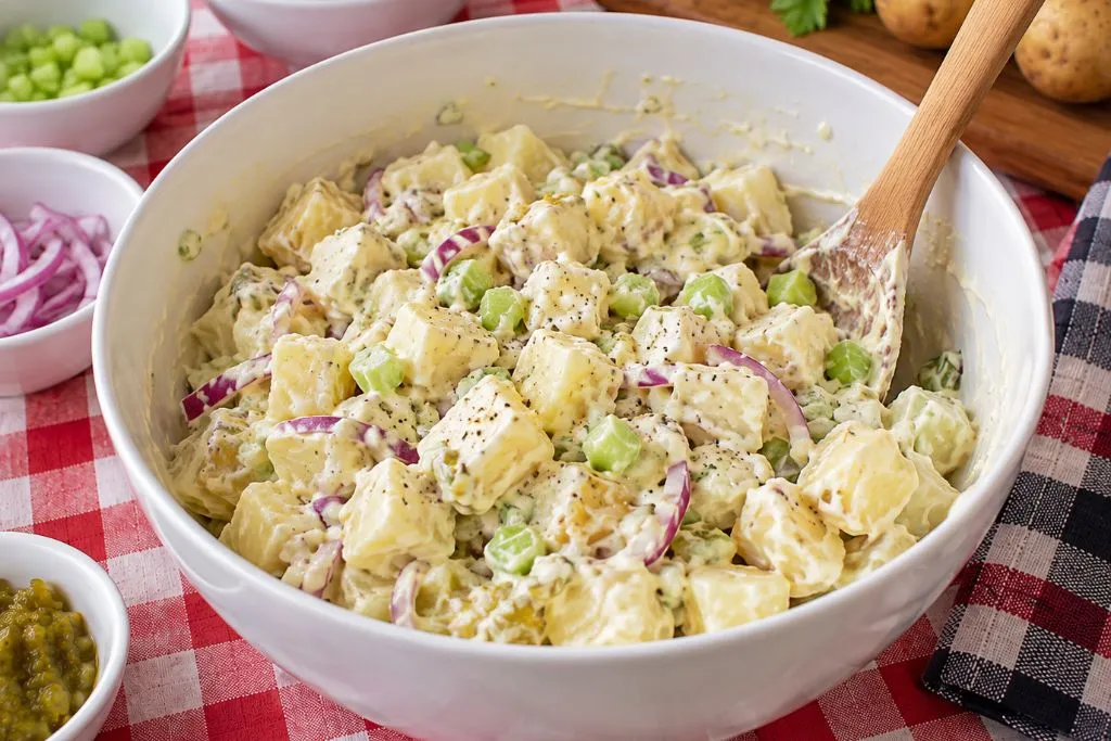 Bowl of classic potato salad mixed with dressing, peas and celery before chilling in the refrigerator
