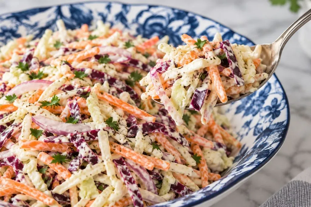 Spoon lifting a scoop of creamy coleslaw with cabbage, carrots and red onion from the bowl